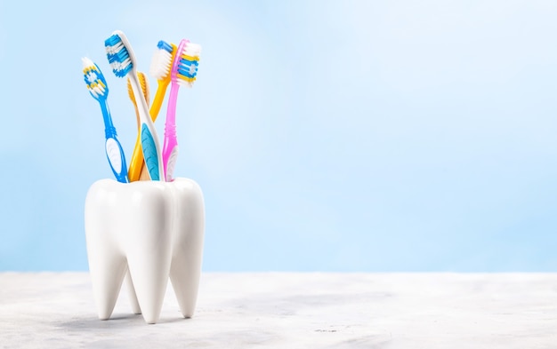 Molti spazzolini da denti in un bicchiere a forma di dente Sfondo blu come scegliere lo spazzolino da denti