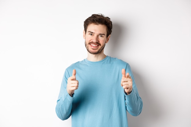 Molto bene. Un bell'uomo sorridente che punta il dito verso la telecamera per congratularsi o elogiare il buon lavoro, sembra orgoglioso, in piedi su sfondo bianco