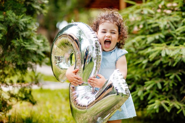 Molto felice bambina di due anni che celebra il suo compleanno ridendo tenendo il numero del palloncino