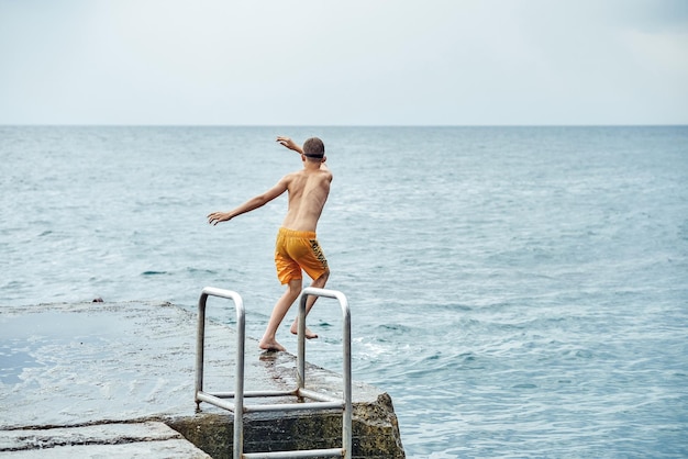 Momenti del ragazzo che salta dal molo di pietra con la scala in mare facendo acrobazie in sequenza di immagini combinate