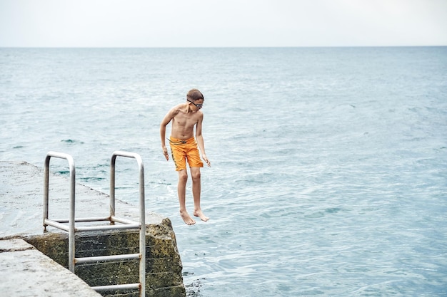 Momenti del ragazzo che salta dal molo di pietra con la scala in mare facendo acrobazie in sequenza di immagini combinate