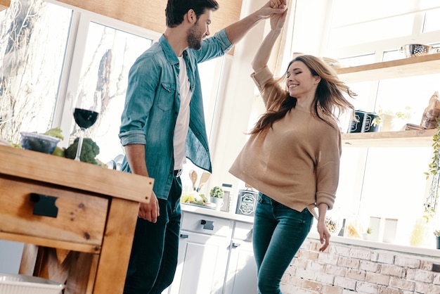 Momenti felici insieme. Integrale di bella giovane coppia in abbigliamento casual che balla e sorride mentre sta in piedi in cucina a casa