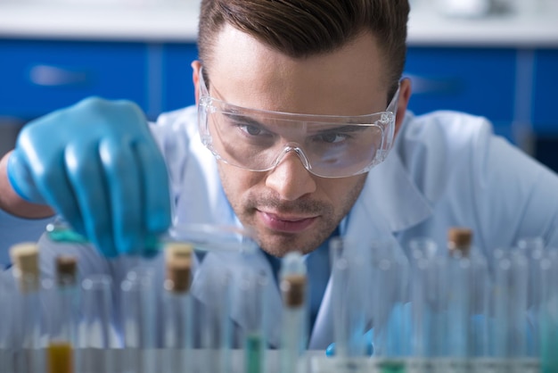 Momento responsabile Giovane serio scopritore di prospettive seduto in laboratorio a lavorare con i tubi di testo e concentrato su quello delle fiale