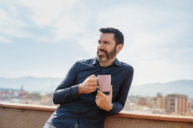 Momento rilassante di un uomo di mezza età in piedi sul balcone a bere caffè