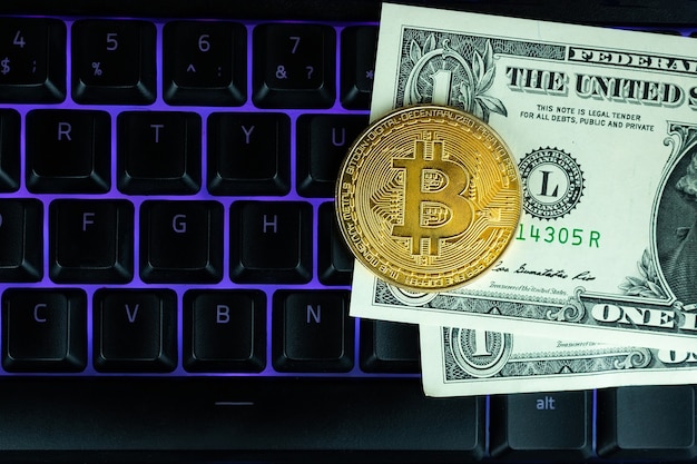 Moneta Bitcoin con laptop e dollari USA. Bitcoin monete d'oro su un portatile di banconote del dollaro ufficio sfondo nero mobile.