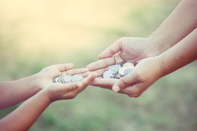 Moneta della tenuta del bambino e della madre in mani come concetto di risparmio dei soldi nel tono d&#39;annata di colore