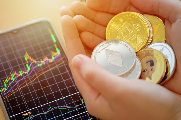 Moneta di valuta digitale nella mano della donna con il telefono che mostra il grafico azionario