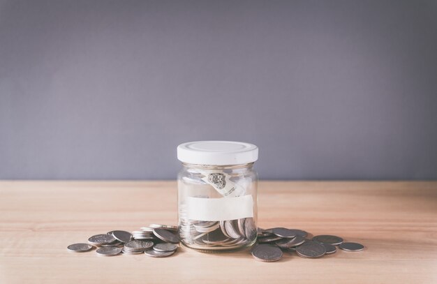 Moneta in un barattolo di vetro con etichetta vuota per il testo su scrivania in legno Concetto di risparmio di denaro