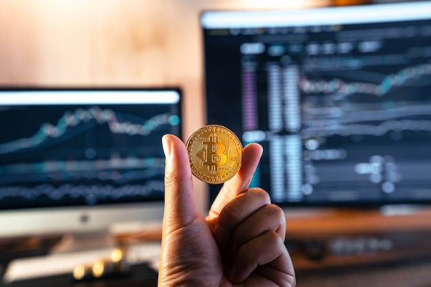 Monete bitcoin in mano davanti al computer e al grafico bitcoin