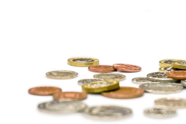 Monete in valuta britannica disposte sparse e ritagliate su sfondo bianco.