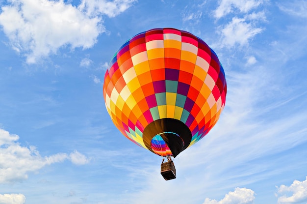 Mongolfiera colorata che vola sopra il cielo blu con nuvole bianche.