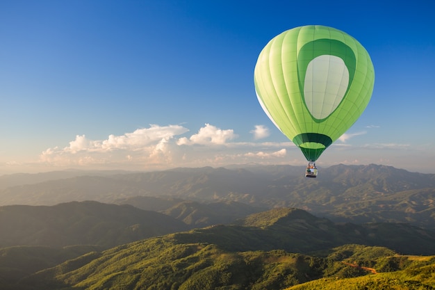 Mongolfiera verde sopra la montagna al tramonto