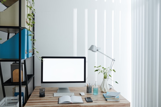 Monitor del computer con schermo vuoto, libri, pianificatore e disinfettante per le mani sul tavolo nell'ufficio domestico della persona