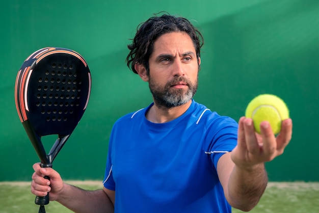 Monitor di padel che tiene una racchetta nera con una pallina da tennis gialla in mano