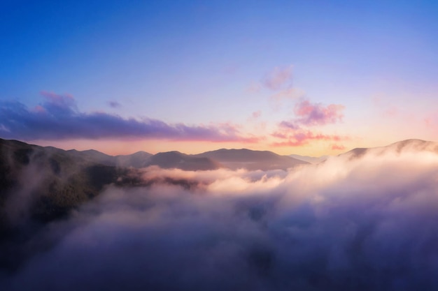 Montagne in nuvole basse Paesaggio di montagna con picchi di cielo nuvoloso drammatici nella nebbia e luce solare intensa all'alba