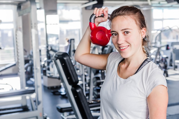 Montare bruna sollevamento kettlebell rosa che sorride alla macchina fotografica in palestra. Foto orizzontale