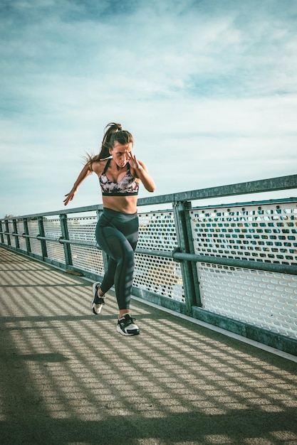 Montare il corridore muscolare della giovane donna che sprinta a grande velocità all'aperto sul ponte del fiume.