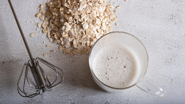 Montare il latte d'avena in un bicchiere e fiocchi d'avena su uno sfondo chiaro