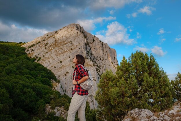 Montare l'escursionista femminile con lo zaino in piedi su una cresta rocciosa di una montagna