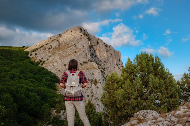 Montare l'escursionista femminile con lo zaino in piedi su una cresta rocciosa di una montagna