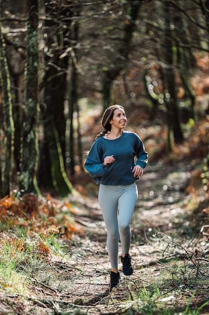 Montare la donna in abbigliamento sportivo che corre lungo il sentiero nella foresta verde