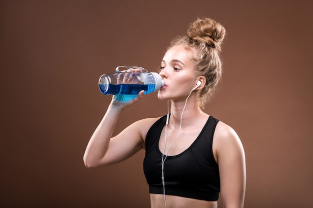 Montare la giovane sportiva assetata in tuta da ginnastica che beve dalla bottiglia di plastica dopo un duro allenamento o fare jogging