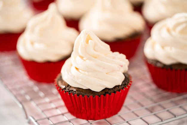 Montare la glassa di crema al burro alla menta piperita sopra i cupcakes al cioccolato e decorare con caramelle di zucchero filato alla menta piperita.