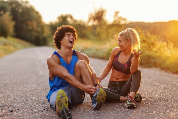 Montare le coppie sveglie che si siedono sulla strada campestre e che riposano dalla corsa. Uomo che lega i lacci delle scarpe. Ora legale al mattino.