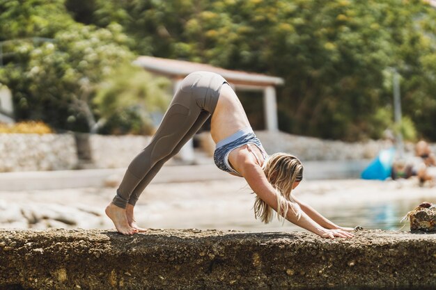 Montare una donna di mezza età che fa esercizi di yoga durante l'allenamento vicino alla spiaggia del mare.