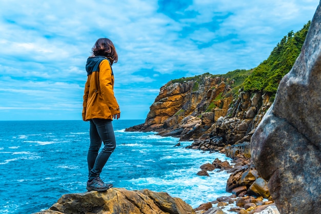 Monte Ulia nella città di San Sebastián, Paesi Baschi. Visita la baia nascosta della città chiamata Illurgita Senadia o Illurgita Senotia. Una giovane donna in una giacca gialla sulle rocce alla ricerca