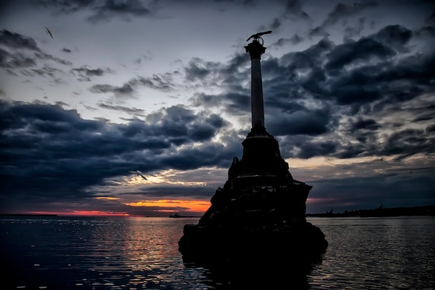 Monumento alle navi da guerra affondate nella baia di Sebastopoli sulla penisola di Crimea. Paesaggio serale. Statua sullo sfondo del tramonto con cielo strutturato e Mar Nero in raggi di sole al tramonto. Luoghi unici in Russia