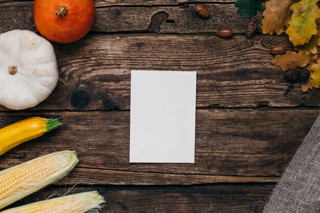 Mood autunnale: carta regalo bianca vuota, zucche e mais con foglie gialle su legno