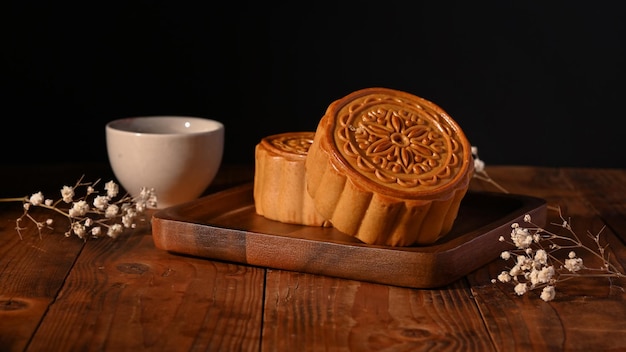 Mooncakes cinesi tradizionali con la tazza di tè e la decorazione con i fiori secchi sulla tavola di legno