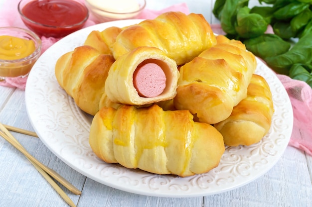 Morbidi panini fatti in casa con salsiccia su un piatto di ceramica su fondo di legno bianco con salse diverse. Salsiccia nell'impasto.