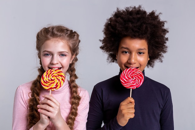 Mordere caramelle dure. Sorridente ragazzo dai capelli scuri con gli occhi neri che mangia caramelle mentre sta con una bella ragazza bionda