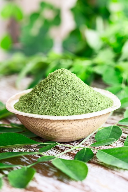 Moringa in polvere (Moringa Oleifera) in una ciotola di cocco con originali foglie fresche di Moringa