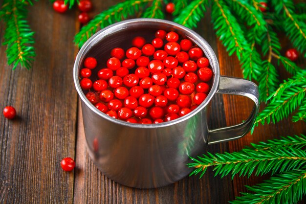 Morse o tè di cowberry in una tazza di latta, circondato da rami di abete su un tavolo di legno.