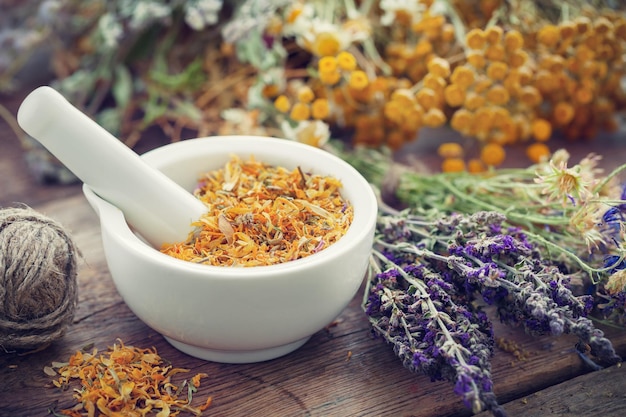 Mortaio di fiori di calendula secchi ed erbe curative su tavola di legno Erboristeria