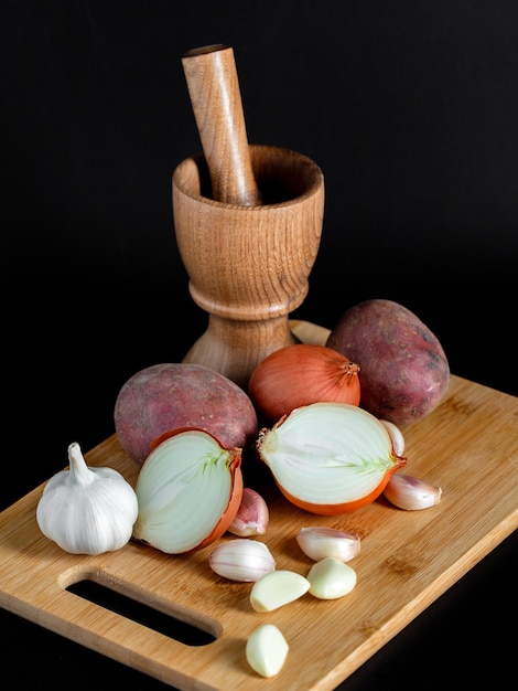 Mortaio di legno (pounder), pestello, cipolla, aglio e altre verdure su nero, utensili da cucina