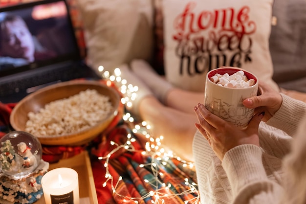 Mosca 29.11.2021. donna che beve una tazza di cacao con marshmallow in mano che tiene e guarda il film "casa da sola" sul laptop a casa in un letto accogliente e cibo popcorn di notte a natale o capodanno