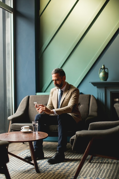 Mostra a mezza età uomo d&#39;affari bere caffè e utilizzando il telefono cellulare nel loby