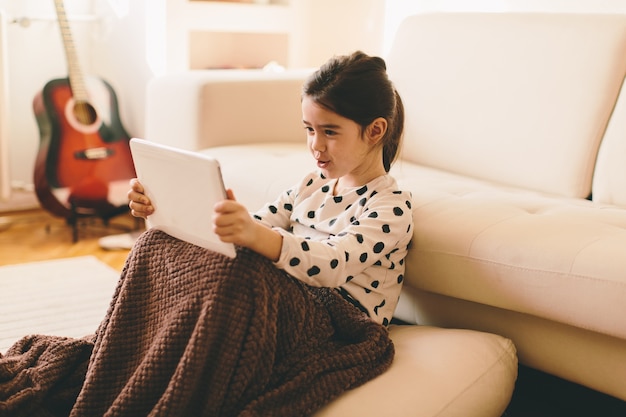 Mostra alla bella bambina che si siede sul pavimento che tiene il tablet