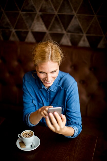 Mostra alla giovane donna che si siede nel caffè, usando il telefono e bevendo caffè