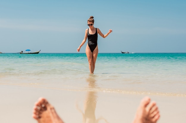 Mostra attraverso le gambe dell'uomo di una bella donna sottile che guarda il mare blu, mare e cielo incredibili.