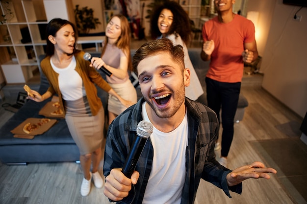 Mostra le tue abilità di canto giovane ragazzo felice che canta con il microfono mentre giochi al karaoke con gli amici