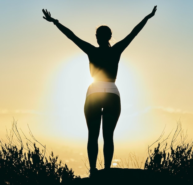 Motivazione natura e silhouette di donna all'alba godendosi la pace mattutina e la libertà sull'oceano Ispirazione calma e schiena della ragazza con le braccia alzate per il culto spirituale benessere e meditazione