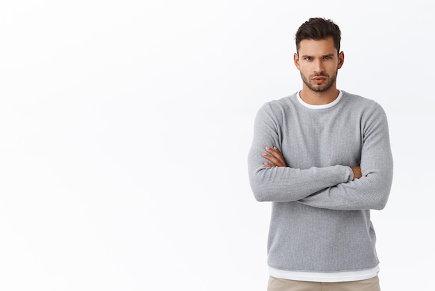 Motivazione persone ed emozioni concetto Seriouslooking determinato bel ragazzo con setole in maglione grigio alla moda sopra la maglietta braccia incrociate petto strabico pensieroso e concentrato