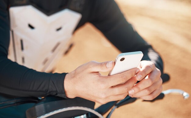 Moto cross telefono e mani dell'uomo su una motocicletta e avventura su strada sterrata all'aperto per lo sport Allenamento fitness e zoom della mano dell'atleta di un giovane SMS o sull'app dei social media per motociclette