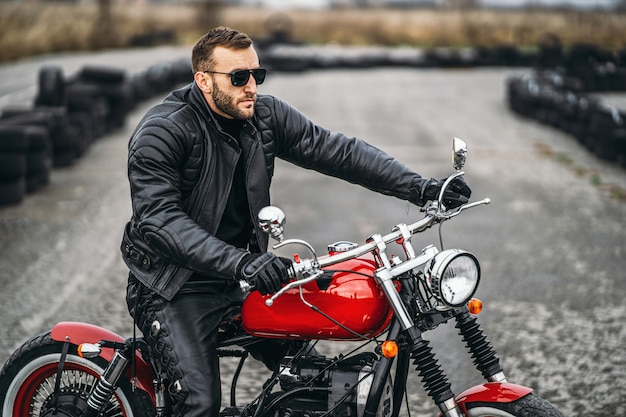 Moto rossa con pilota. Un uomo con una giacca di pelle nera e pantaloni si trova lateralmente in mezzo alla strada. I pneumatici sono posati sullo sfondo