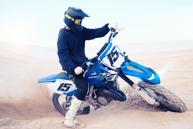 Motocicletta sporca e atleta che guida in avventure sportive o uomo nella sabbia del deserto e che cavalca all'aperto su dune nella natura Guida sportiva estrema in bici o in moto con casco o persona in libertà
